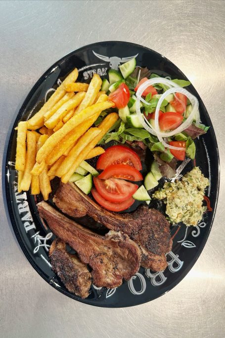 Ein schwarzer Teller mit Pommes, Salat, Tomaten, Gurken und gebratenem Fleisch.